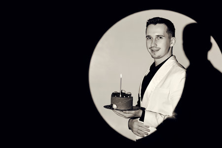 elegant caucasian man in white suit tuxedo holding cake with candle in the circle of light, copy space. Celebrationの写真素材