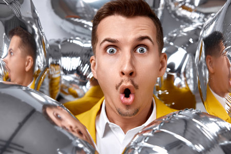 portrait of surprised man in yellow jacket with a lot of silver air balloons. birthday partyの写真素材