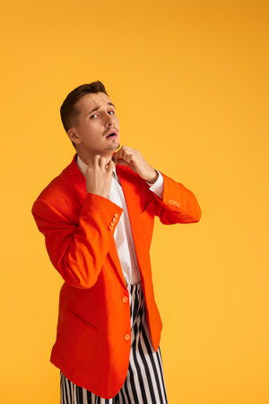 Cheerful funny young man in orange jacket and striped pants on yellow background.の写真素材