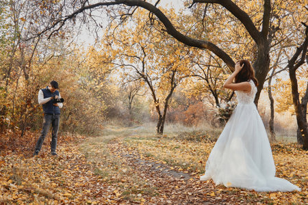Professional wedding photographer taking pictures of the bride and groom in nature in autumnの写真素材