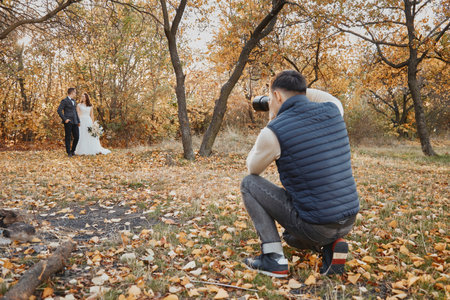 Male wedding photographer taking pictures of the bride and groom in nature in autumnの写真素材