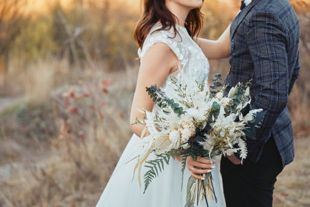 bride and groom holding beautiful bouquet in nature in autumnの写真素材