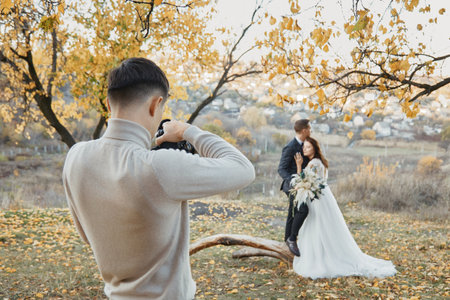 Professional wedding photographer taking pictures of the bride and groom in nature in autumnの写真素材