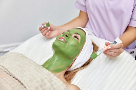 female beautician applies the mask to the face of beautiful woman in the spa salon. facial skin careの写真素材