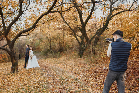 Professional wedding photographer taking pictures of the bride and groom in nature in autumnの写真素材