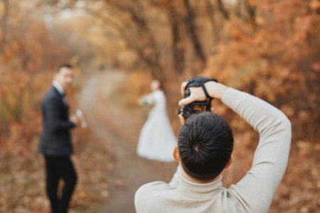 Professional wedding photographer taking pictures of the bride and groom in nature in autumnの写真素材