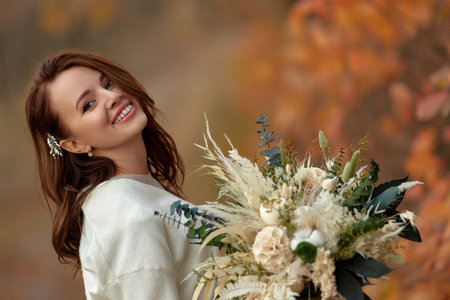 portrait of beautiful happy bride holding wedding autumn bouquet in natureの写真素材