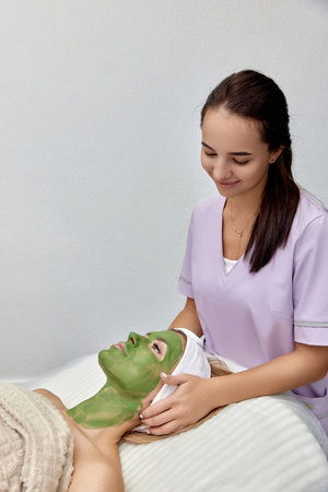 female beautician applies the mask to the face of beautiful woman in the spa salon. facial skin careの写真素材
