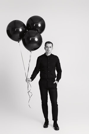 elegant caucasian man with bunch of black air balloons on white background. black and whiteの写真素材