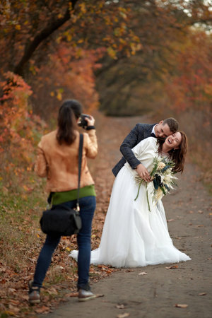 female wedding photographer taking pictures of the bride and groom in autumnの写真素材