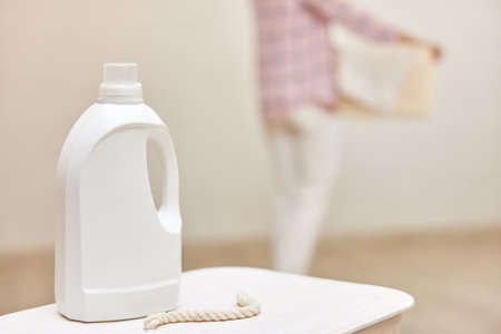 washing gel or fabric softener on white laundry basket against the background of blurred woman with basket of laundry . Mock up, copy space.の写真素材