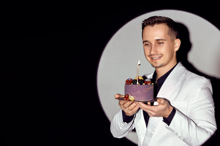 elegant caucasian man in white suit tuxedo holding cake with candle in the circle of light, copy space.の写真素材