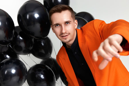 handsome man in orange jacket with black air balloons on white background. birthday partyの写真素材