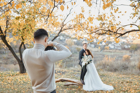 Professional wedding photographer taking pictures of the bride and groom in nature in autumnの写真素材