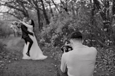 Professional wedding photographer taking pictures of the bride and groom in nature in autumnの写真素材