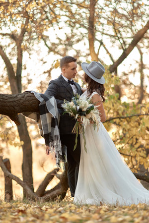 beautiful happy stylish bride in hat and groom hugging outdoor in autumnの写真素材