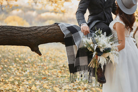 bride and groom kissing and holding beautiful bouquet in nature in autumnの写真素材