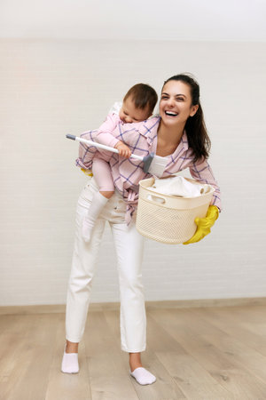 happy mother housewife is holding cute baby girl and basket with laundry and doing housework, Happy family having funの写真素材