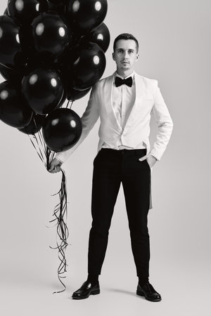 elegant caucasian man in white suit tuxedo with black air balloons on white background.の写真素材