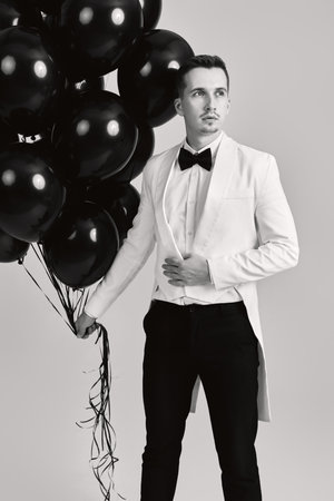 elegant guy in white suit tuxedo with black air balloons on white background. holiday celebrationの写真素材