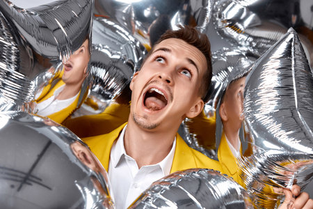 portrait of happy man in yellow jacket with a lot of silver air balloons. birthday partyの写真素材