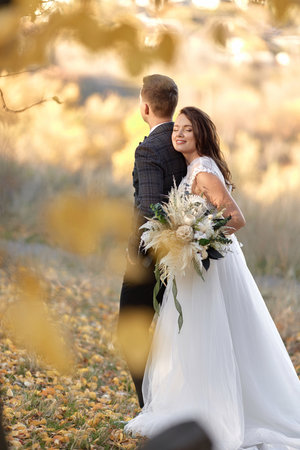 beautiful sensual bride in white wedding dress holding bouquet and embracing groom outdoor on natural backgroundの写真素材
