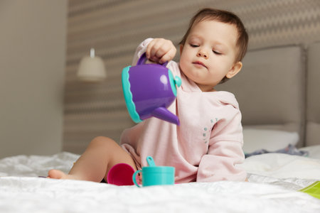 happy cute little child girl playing with tea toy cups on bedの写真素材