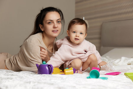 mother and cute little child daughter playing tea party and spending time together in bedroomの写真素材