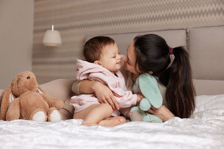 happy mother and her little child daughter playing with bunny toys in bedroom, family having funの写真素材