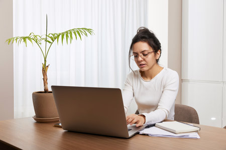 pretty woman in glasses using laptop and communicates with customer on internet at homeの写真素材