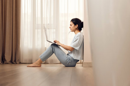 casual woman sitting on the floor and working on laptop at homeの写真素材