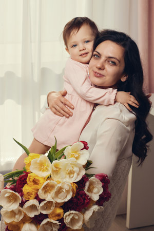 Cute little baby daughter and mom with flowers tulips. Mother and child hugging. Happy mothers day.