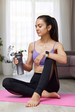 athletic fitness woman drinking water sitting on pink exercise mat at homeの写真素材