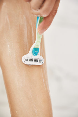 Young woman shaving her legs with razor in white shower, close-upの写真素材