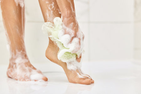 Woman washing her legs with foam bubbles and bath sponge while taking shower in the bathroomの写真素材