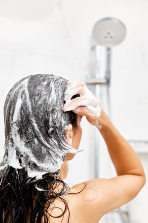 Young woman taking refreshing shower in marble bathroom. Girl washing her hair, back viewの写真素材