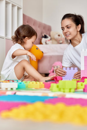 cute baby girl and her loving mother build tower from colorful cubes, having fun togetherの写真素材