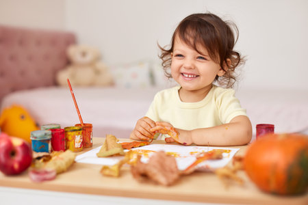 happy little child girl painting autumn leaves. baby girl drawing leaves in yellow and orange paintの写真素材