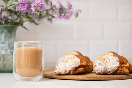 Delicious fresh croissants on wooden tray and glass of coffee on white table, closeup, tasty breakfastの写真素材