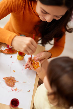 Cute little girl and mom spending good time painting hands and autumn yellow leaves togetherの写真素材