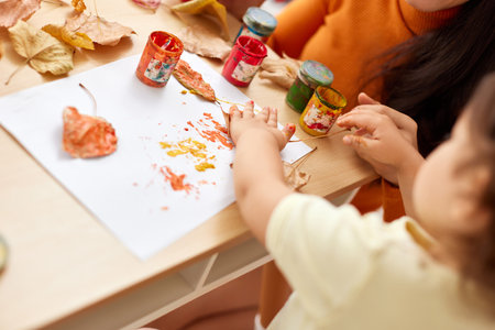close-up, child and mom hands painting autumn yellow leaves together. happy time together at homeの写真素材