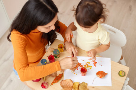 Cute little girl and mom spending good time painting autumn yellow leaves togetherの写真素材