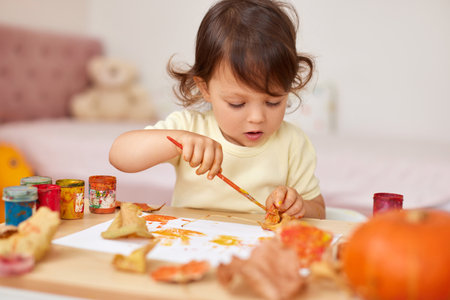 cute little child girl painting autumn leaves. baby girl drawing leaves in yellow and orange paintの写真素材