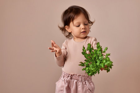 smiling child girl holding fresh green parsley on beige background. healthy baby food.の写真素材