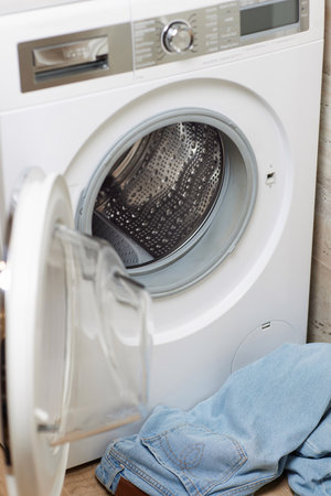 dirty jeans near open washing machine in laundry room.