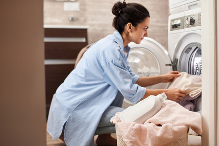 woman put pastel cotton towel in automatic washing machine with open door in bathroomの写真素材