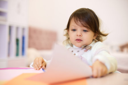 little child girl holding multi-color paper while sitting by table at home, Children creativityの写真素材