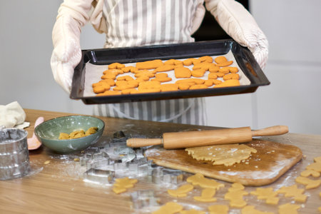 housewife woman in apron holds cookies on baking tray in kitchenの写真素材