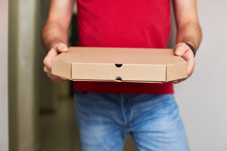 delivery man in red t-shirt giving food order and holding pizza box at home.の写真素材
