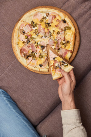 male hand takes a piece of delicious pizza from wooden plate, top view